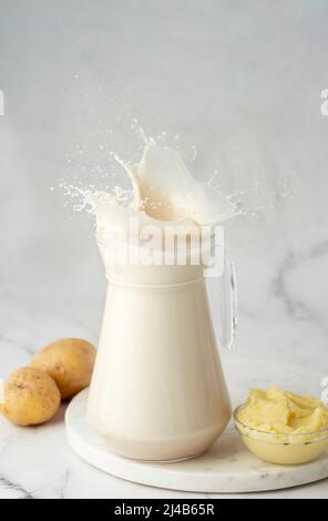 Éclaboussures de lait de pomme de terre dans un pot en verre sur fond de marbre blanc. Lait végétalien dans un pot en verre avec purée de pommes de terre et tubercules de pommes de terre sur le fond. Copier l'espace. H Banque D'Images