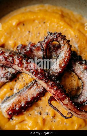 Gros plan de tentacules de pieuvre grillée, purée de patate douce, sur un bol beige. Banque D'Images