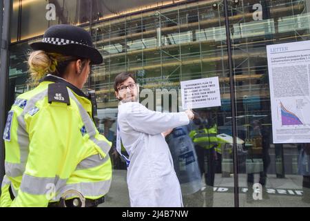 Londres, Angleterre, Royaume-Uni. 13th avril 2022. Un scientifique avec sa main surcollée à la fenêtre explique pourquoi ils protestent contre un policier. Les scientifiques se sont collés au ministère des Affaires, de l'énergie et de la Stratégie industrielle pour protester contre les combustibles fossiles et exiger que le gouvernement agisse sur le changement climatique. Cette action s'inscrivait dans le cadre des manifestations de la rébellion contre l'extinction qui ont lieu autour de la capitale. (Credit image: © Vuk Valcic/ZUMA Press Wire) Credit: ZUMA Press, Inc./Alamy Live News Banque D'Images