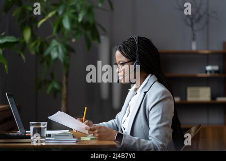 Jeune femme afro-américaine spécialiste du service clientèle à distance en micro-casque/oreillette travaillant à domicile Banque D'Images