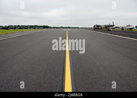 Ligne jaune centrale sur la ligne de taxi de l'aérodrome avec les avions de la Seconde Guerre mondiale garés de chaque côté au spectacle aérien, Biggin Hill, Kent, Angleterre Banque D'Images