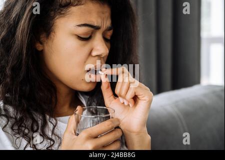 Gros plan d'une jeune femme afro-américaine, prenez une pilule à cause d'avoir des maux de tête. Belle femme malsaine souffrent de stress ou de maladie. Une femme afro-américaine attrape un rhume ou une grippe Banque D'Images