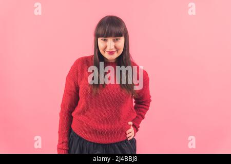 Moyenne prise de vue jolie jeune femme caucasienne regardant la caméra et souriant, en gardant une main sur la taille rose fond isolé copie espace studio tourné . Photo de haute qualité Banque D'Images