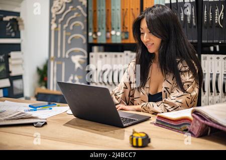 Khabarovsk, Russie, Desember 16, 2021. Happy Asian femme designer d'intérieur professionnel de travail utiliser l'ordinateur portable dans le studio de bureau Banque D'Images