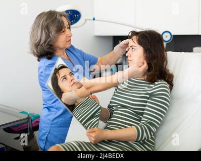 Un médecin expérimenté en cosmétologie examine le visage d'une jeune femme patiente Banque D'Images
