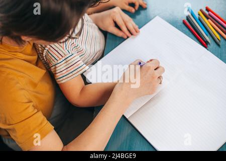 Vue de dessus d'une mère aidant son enfant de fils avec des devoirs et des exercices. Difficultés de préparation à l'école et d'apprentissage écrire et dessiner. Famille Banque D'Images