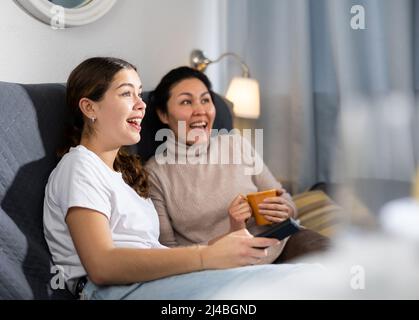 Deux amies qui regardent la télévision tout en étant assise sur un canapé à la maison Banque D'Images