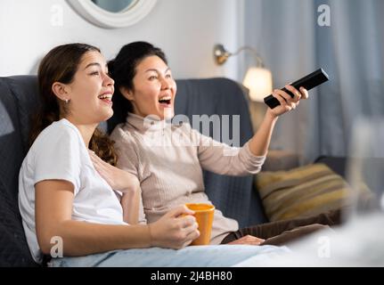 Deux amies qui regardent la télévision tout en étant assise sur un canapé à la maison Banque D'Images