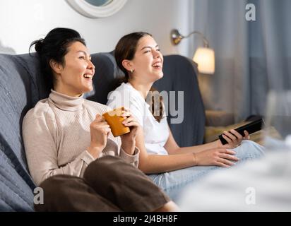 Deux amies qui regardent la télévision tout en étant assise sur un canapé à la maison Banque D'Images