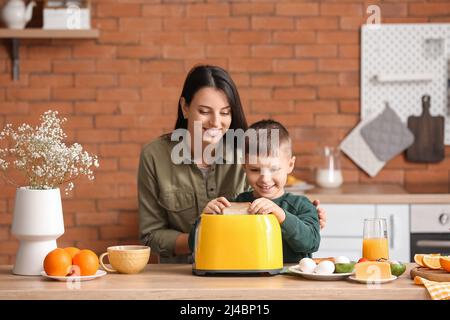 Petit garçon avec sa mère mettant des tranches de pain dans le grille-pain dans la cuisine Banque D'Images