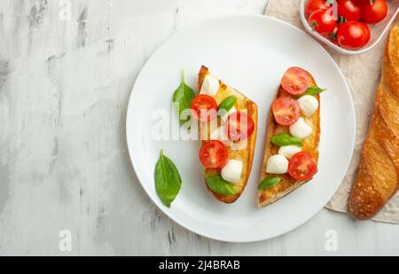 Bruschetta aux tomates, mozzarella et basilic dans une assiette blanche. En-cas ou en-cas italiens traditionnels, antipasti. Avec espace pour l'écriture Banque D'Images