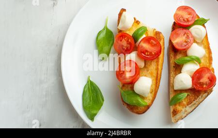 Bruschetta aux tomates, mozzarella et basilic dans une assiette blanche. En-cas ou en-cas italiens traditionnels, antipasti. Avec espace pour l'écriture Banque D'Images