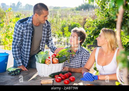 Famille souriante discutant avec un petit sourire à une table en bois dans le jardin Banque D'Images