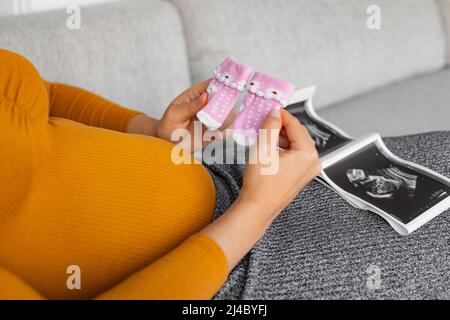 Femme enceinte regardant l'échographie de sexe révèle son un bébé fille tenant des chaussettes roses nouveau-né attendant la naissance de son enfant. D'abord Banque D'Images