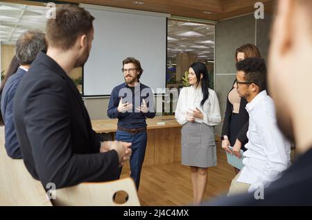 Coach d'affaires créatif parlant à l'équipe d'entrepreneurs qui sont debout dans le bureau autour de lui Banque D'Images