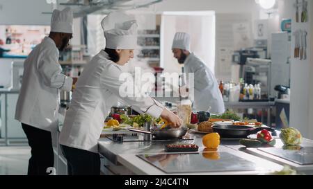 Chef professionnel préparant l'ingrédient de poivron sur la planche à découper, ajoutant des légumes sur le plat de repas gastronomique. Femme authentique cuisant des plats délicieux dans la cuisine du restaurant. Prise de vue à main levée. Banque D'Images