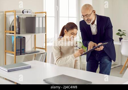 La femme heureuse met sa signature sur le contrat que le courtier de prêt ou l'agent immobilier lui donne Banque D'Images