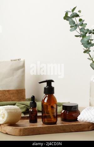 Bouteilles de cosmétiques en verre ambré brun sur plateau en bois sur table avec sac de cosmétiques et eucalyptus. Ensemble de produits de beauté luxueux pour salle DE bain SPA. Banque D'Images
