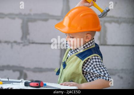 Portrait de petit constructeur en casques avec instruments pour la rénovation sur la construction. Garçon de créateur, enfant de menuisier avec ensemble d'outils de constructeur. Enfants Banque D'Images