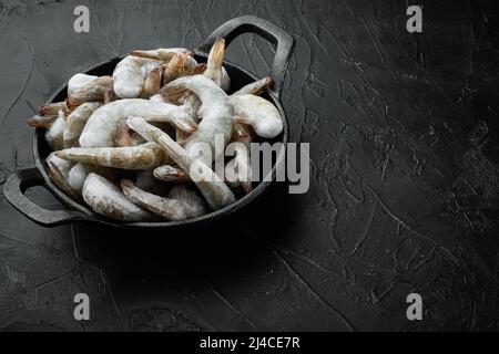 Crevettes tigrées crues non cuites congelées, set de crevettes, dans une poêle en fonte, sur fond de pierre noire, avec espace de copie pour le texte Banque D'Images