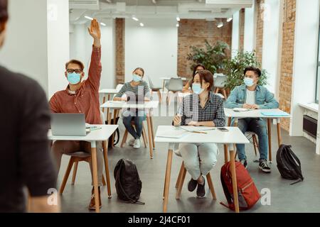 Jeune homme dans le masque de protection du visage levant la main pour la réponse Banque D'Images