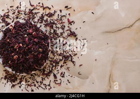 Séchez le thé à l'hibiscus dans un bol. Calyces d'hibiscus séchés, tisane à base de cramoisi et de sepals de couleur magenta profond de la fleur de roselle, dans le bol sur t Banque D'Images