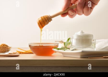 Crème avec extraits de miel et main avec bâton montrant le miel et la cire d'abeille sur une table en bois et un fond isolé. Composition horizontale. Vue avant. Banque D'Images
