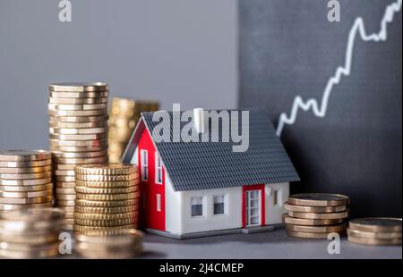 Maison avec des piles d'argent et une courbe montante symbolisant la hausse des prix immobiliers Banque D'Images