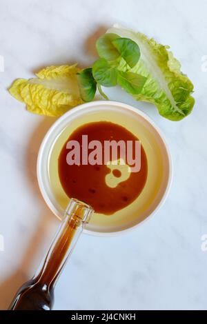 Bol avec huile de cuisson et aceto balsamico, bouteille avec vinaigre, feuilles de salade Banque D'Images