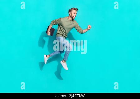 Photo de tout le corps de jeune homme blond saut avec ordinateur portable pull jeans baskets isolées sur fond turquoise Banque D'Images