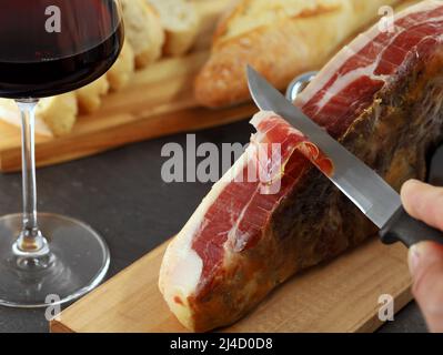 Main mâle avec couteau coupe le jambon Jamon Serrano original en tranches, gros plan, Banque D'Images