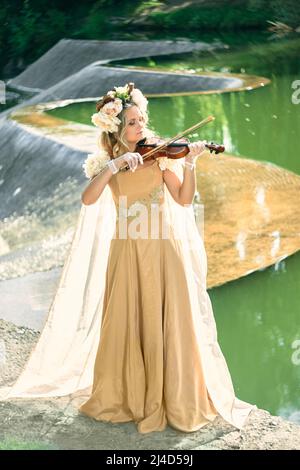 femme en robe joue le violon près d'une cascade Banque D'Images