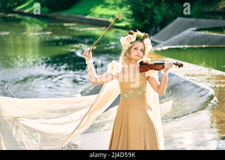 femme en robe joue le violon près d'une cascade Banque D'Images