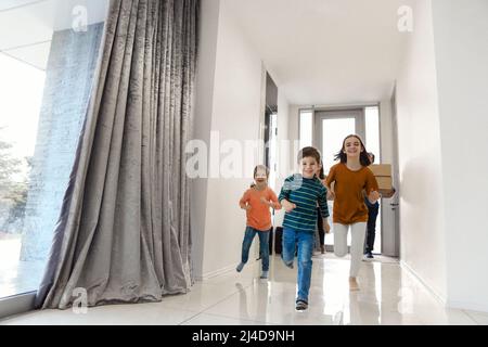 Bonne famille dans le hall. Drôle d'enfants sautant avec boîte de carton, les parents riant, jouer avec les enfants ont plaisir ensemble déplacer à la nouvelle maison. Hypothèque Banque D'Images