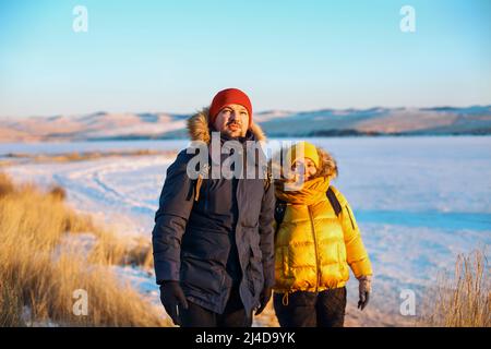 Couple romantique de touristes vêtus de vêtements de sport chauds d'hiver avec des sacs à dos touristiques marchant dans les montagnes enneigées dans un incroyable coucher de soleil. Ogoi isla Banque D'Images