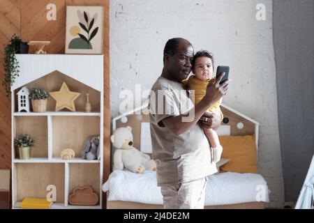 Portrait d'un père afro-américain mûr heureux tenant une belle fille de bébé prenant des photos de selfie sur l'appareil photo de smartphone Banque D'Images