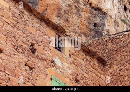 Mur de pierre épais de bâtiment médiéval avec une pente de toit en tuiles et une petite fenêtre barrée dans l'ancien village de Peyre, France Banque D'Images