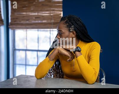 Young African American Woman avec chemise jaune assis au comptoir de la cuisine de l'île. Image style ethnique très tendance. Banque D'Images