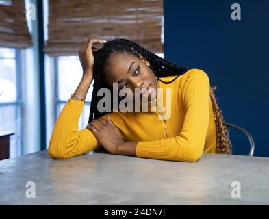 Young African American Woman avec chemise jaune assis au comptoir de la cuisine de l'île. Image style ethnique très tendance. Banque D'Images