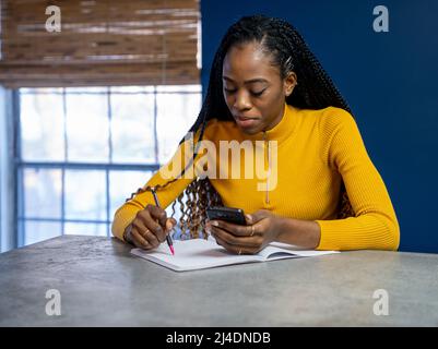 Young African American Student avec chemise jaune assis au comptoir de la cuisine island écrit sur un ordinateur portable. Image style ethnique très tendance. Banque D'Images