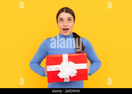 fille stupéfait tenant boîte cadeau après avoir fait des achats sur fond jaune, acheter Banque D'Images