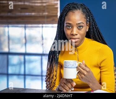 Young African American Student avec chemise jaune assis au comptoir de la cuisine island écrit sur un ordinateur portable. Image style ethnique très tendance. Banque D'Images