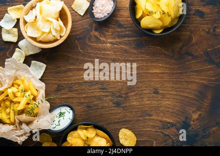 Aliments ou collations malsains. Tous les en-cas classiques de pommes de terre avec des arachides, du pop-corn et des rondelles d'oignon et des bretzels salés dans des assiettes à bol sur fond de bois ancien. Banque D'Images