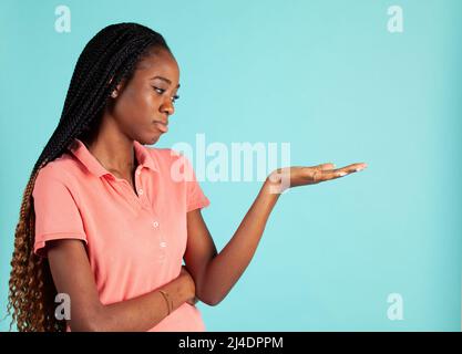 Femme africaine américaine avec palmier bouleversée. La porte-parole pose en tenant votre produit dans la paume de sa main. Banque D'Images