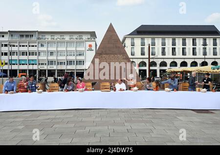 Karlsruhe, Allemagne. 14th avril 2022. Douze disciples modernes s'attardent à une table sur la place du marché, représentant 'la Cène' comme une version contemporaine et vivante de la peinture de Léonard de Vinci. L'œuvre œcuménique de l'église de la ville 'Fächersegen' à Karlsruhe a invité à un repas de paix sur la place du marché. À la « Table de la paix » de onze mètres de large, les disciples modernes - jeunes, vieux, femmes, hommes et un bébé de différents pays - ont distribué du pain aux passants le jeudi Maundy avec les mots « la paix soit avec vous ». Credit: Uli Deck/dpa/Alay Live News Banque D'Images