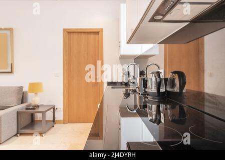 cuisine américaine avec dessus en marbre noir avec petits électroménagers, plaque vitrocéramique à quatre brûleurs, canapé en tissu et table d'appoint grise Banque D'Images