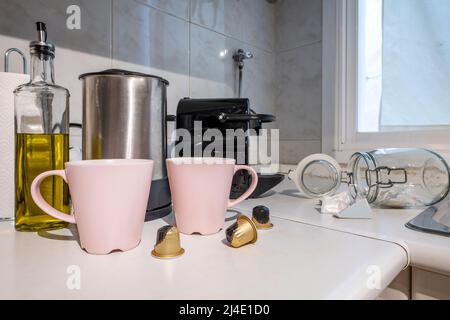 Coin d'une cuisine avec une machine à café à dosettes à côté de tasses rose pâle à côté d'une bouilloire en acier inoxydable et d'une burete à huile Banque D'Images