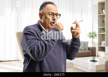 Homme mature fumant et toussant à la maison dans un salon Banque D'Images