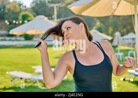 Mature belle femme en maillot de bain relaxant en été, peignant ses cheveux avec peigne Banque D'Images