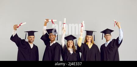 Heureux diplômés divers de collège ou d'université en casquettes et robes de possession de leurs diplômes Banque D'Images